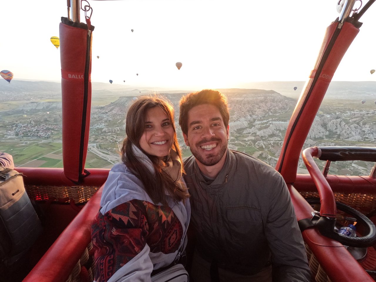 Joana and João in a hot-air balloon basket above Cappadocia at sunrise.